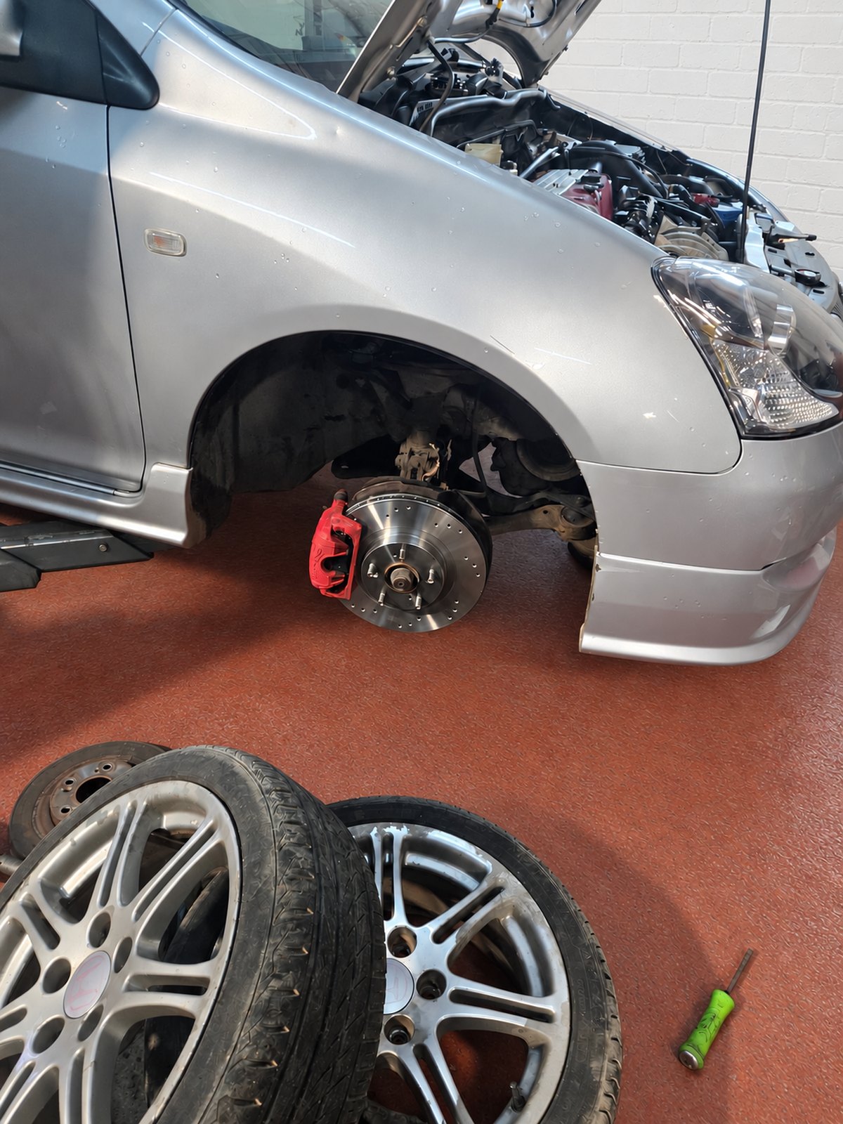 Car with its front wheel off and brakes exposed during a repair